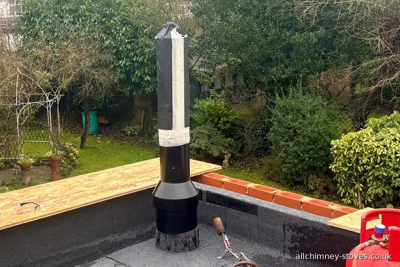 HETAS certified twin wall flue installation — 125mm insulated flue first fix rising through flat roof extension, weathering plate being torched, solid fuel cowl to follow, Allchimney Stoves, Gidea Park Romford